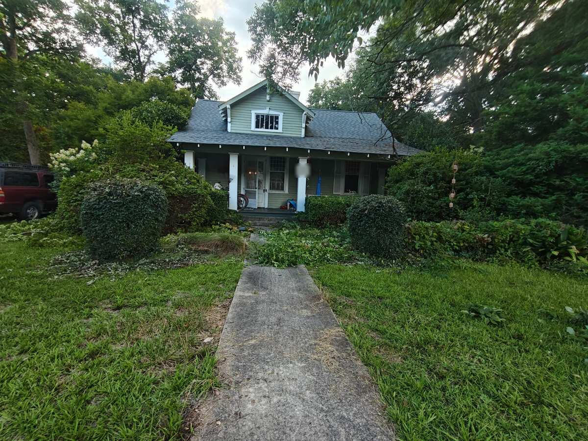 Overgrown front beds and ground cover along the walkway of a bungalow in Winterville, GA, before cleanup